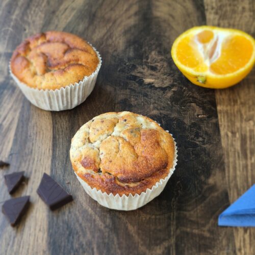 Muffins auf einem Holztisch mit blauer Serviette, Schokolade und Mandarinen.